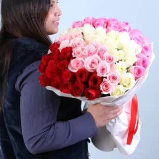 Bouquet featuring ombre red, pink and white roses in layered white wrapping with red satin ribbon.