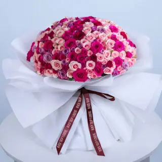 Bouquet featuring dark pink & peach spray roses with pink roses and purple roses in premium white wrap.