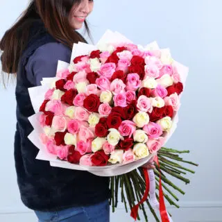 Bouquet featuring red, pink and white roses in layered white wrapping with hand-tied stems.