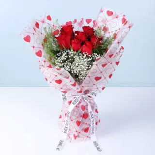 Bouquet of 7 red roses, gypsophila, and lipidium in heart-print wrapping.