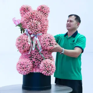 Light pink spray roses in a teddy arrangement style, finished with a white ribbon.