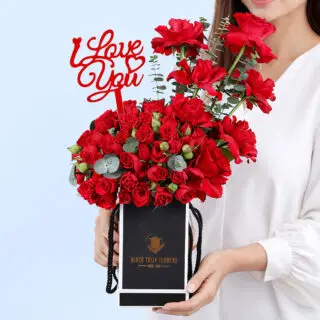 Valentines magic featuring classic red roses, red spray roses, and fresh eucalyptus arranged in a compact premium black box