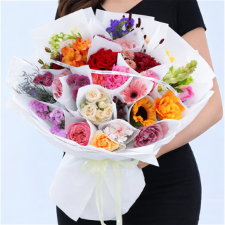A bouquet featuring mixed roses, sunflower, carnations, lisianthus, chrysanthemums and statice in a white wrap.