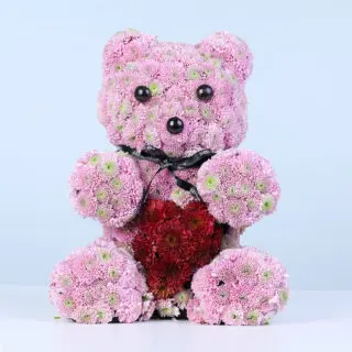 Purple chrysanthemums and red spray roses arranged as a flower teddy holding a heart detail, finished with a ribbon.