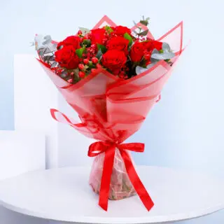 A bouquet of red roses, eucalyptus leaves and red hypericum in a bold red translucent wrapping.