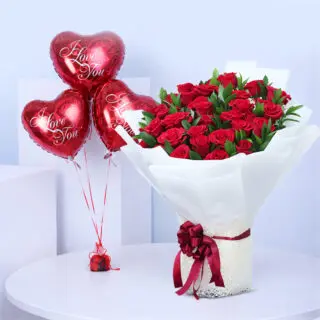 Red roses and green foliage in a white wrap, paired with red heart balloons printed “Love You”.