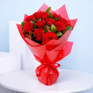 Hand-tied bouquet of red roses and red chrysanthemums accented with baby’s breath, eucalyptus, and green berries, presented in bold red wrapping.