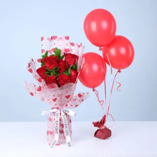Bouquet of red roses and green foliage in a heart-print wrap, paired with three red balloons.