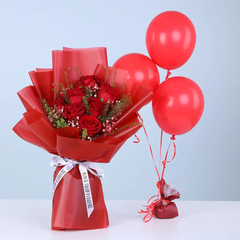 Bouquet of red roses with baby’s breath and green fillers in red wrapping, with three red balloons.