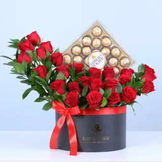 A black round box featuring 25 red roses and ruscus foliage paired with Ferrero Rocher