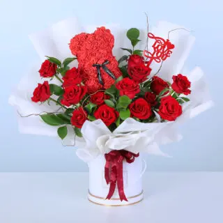Red roses with ruscus in a white box with a rose teddy topper, finished with a “Love You” message.