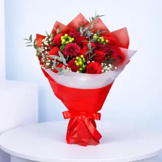 Red roses, red chrysanthemums, baby’s breath, eucalyptus and green berry accents in bold red wrapping.