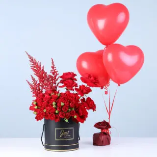 A black box featuring red spray roses and red blooms paired with three red heart balloons.