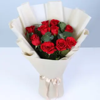 A bouquet of red roses and eucalyptus accents, elegantly wrapped and finished with a satin ribbon.