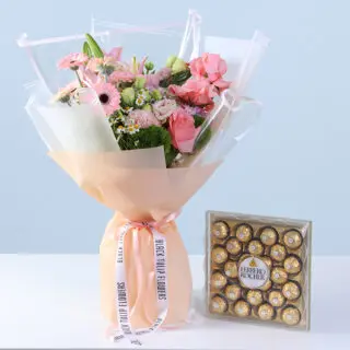 Pink roses, gerberas, lilies, and seasonal blooms in soft peach wrapping, finished with a ribbon bow and paired with a 24-piece Ferrero Rocher chocolate box.