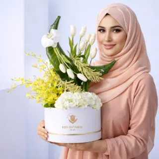 Crescent floral arrangement with white tulips, orchids, hydrangeas, and tropical leaves in silver box.