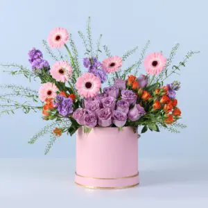 A vibrant floral arrangement featuring pink, purple, and orange blooms styled in a structured pink gift box with a full, colourful presentation.