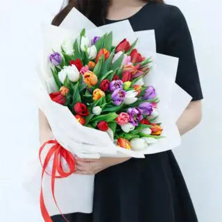 Mixed tulip bouquet with vibrant colours wrapped in white decorative paper and tied with a red satin ribbon.