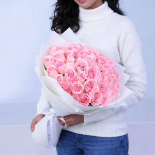 A sophisticated bouquet of gentle pink roses, elegantly wrapped and tied, showcases a full, lush floral display.