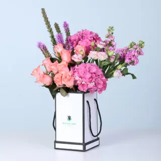 Elegant pastel floral arrangement in a modern white box containing pink Matthiola, Hydrangea, Lisianthus, orange roses, and purple flowers. Designed for gifting and special occasions