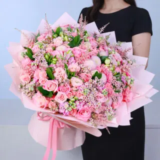 Mixed pink flower bouquet showcasing roses, lisianthus, alstroemeria, matthiola, astilbe, and delicate filler flowers arranged with fresh foliage. Wrapped in a pink sheet and been tied with satin ribbon.