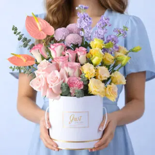 Pink roses, purple matthiola, peach anthurium, purple ping pong blooms, peach lisianthus, and eucalyptus in a white luxury round box, finished with a Just For You message label.