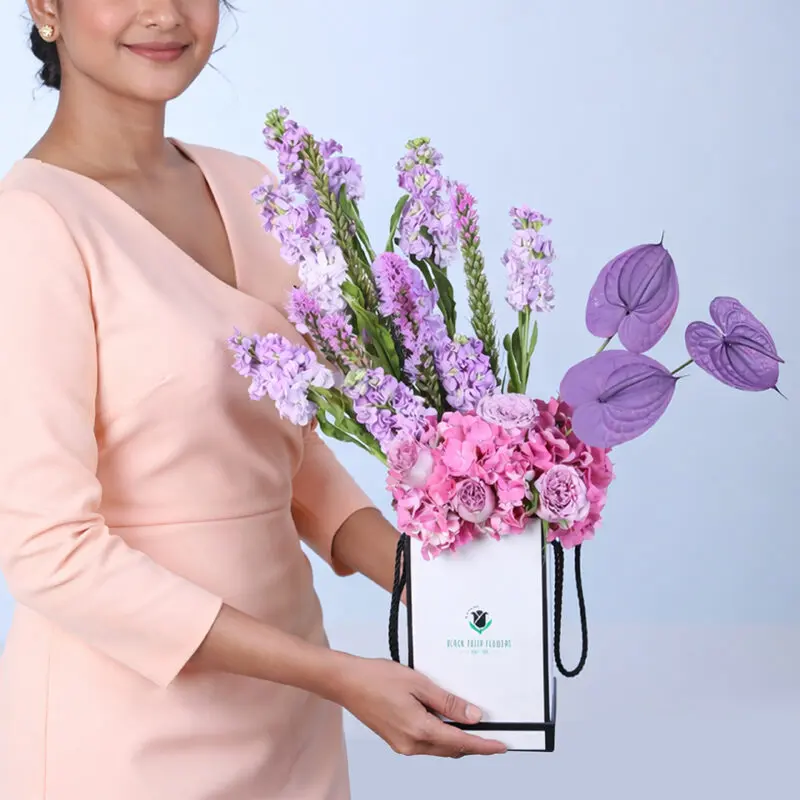 A purple floral arrangement with Mattiolla, Anthurium, Hydrangea, Liatris, and Roses, presented elegantly in a sleek white box.