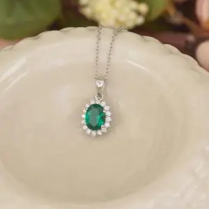 a silver necklace with a pendant. The pendant has a large, oval-cut emerald surrounded by smaller, clear gemstones