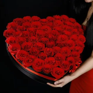 A heart-shaped black box filled with vibrant red roses, elegantly tied with a red ribbon.