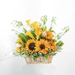 A wicker basket filled with a vibrant arrangement of sunflowers, lilies, and greenery.