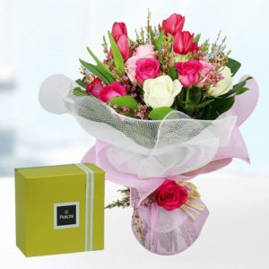 A bouquet of pink roses, white roses, and pink tulips wrapped in a white mesh with a pink ribbon. A yellow gift box is next to the bouquet.