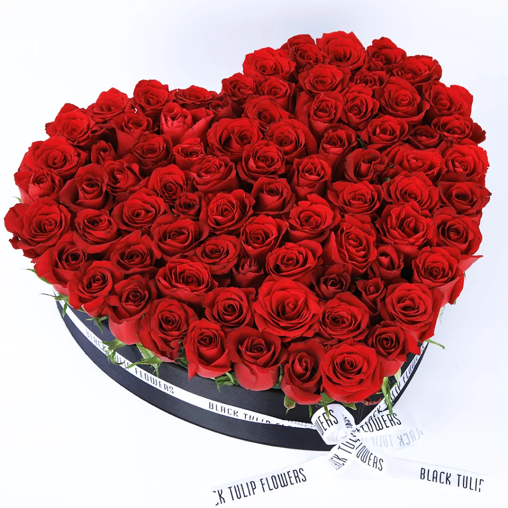 BT_FL_2025 A heart-shaped black box filled with 80-100 exquisite red roses, elegantly adorned with a white ribbon.
