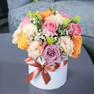 Colourful roses with gypsophila and greenery in a white box, tied with a brown ribbon.