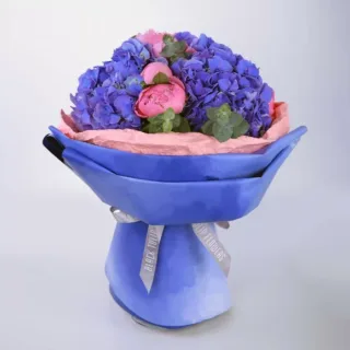 A bouquet of pink peonies and blue hydrangeas wrapped in blue paper.