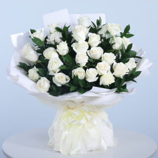 Bouquet of 30 white roses with fresh green leaves in a white wrap and tied with a white ribbon.