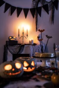 A Halloween-themed room decorated with pumpkins, candles, a ghost costume, and black and white bunting.