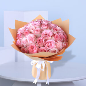 A bouquet of pink roses wrapped in brown paper with a white ribbon.