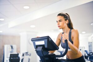 A woman exercises on a stationary bike in a gym, focusing on her fitness routine amidst a modern workout environment.