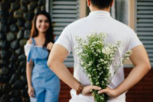 A man presents a bouquet of flowers, while a woman stands gracefully behind him, creating a moment of affection.