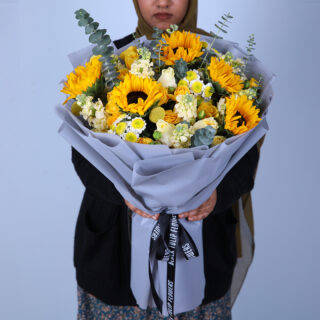 A bouquet of sunflowers, roses, and daisies in a gray paper wrapper.
