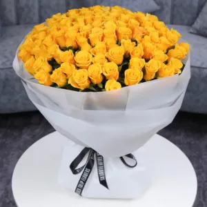 A large bouquet of bright yellow roses wrapped in white paper with a black ribbon.