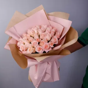 A romantic bouquet of light peach roses, ready for gifting, being held by a person with a focus on the soft color and the elegant wrapping.