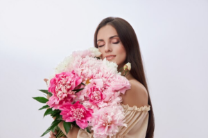 A beautiful woman holding a bouquet of pink and white flowers, radiating joy and elegance in a serene setting.