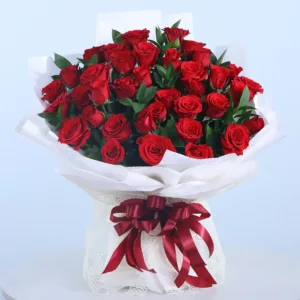 A lush bouquet of red roses is presented in a white paper wrapping, tied with a deep red ribbon.