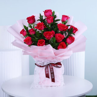 Dark pink rose bouquet with greenery wrapped in pink and finished with a maroon ribbon.
