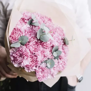 a bouquet of pink carnations wrapped in light brown paper, held by a person wearing a white shirt