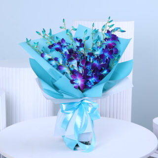 A hand-tied bouquet of vibrant blue dendrobium orchids with fresh green leaves, wrapped in light teal paper and tied with a light blue ribbon.
