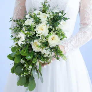 Elegant bridal bouquet with white garden roses, wax flowers, and lush green foliage arranged for modern wedding ceremonies.