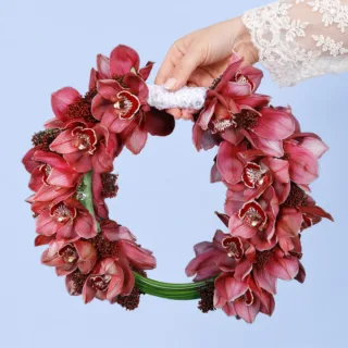 Luxury red orchid bridal bouquet with vibrant cymbidium blooms, textured skimmia accents, and flowing steel grass greenery.