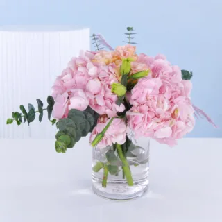 Cylindrical glass vase centerpiece featuring soft pink hydrangeas and lisianthus arranged for elegant table decor and refined event styling.